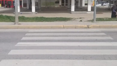 Fotoğrafta, bir yaya geçidi ve karşısında terkedilmiş gibi görünen bir benzin istasyonu bulunuyor. Yaya geçidi, kaldırımın yüksek olması nedeniyle engelli ve yaşlı bireyler için erişilebilir görünmüyor. Yolun karşısında bir kişi yürürken görülüyor.