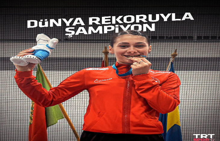 Görselde, kırmızı milli takım eşofmanı giymiş genç bir kadın sporcu, madalyasını ısırarak zaferini kutluyor. Bir elinde maskot oyuncak, diğer elinde madalyası bulunuyor. Arkada çeşitli ülke bayrakları yer alıyor. Üst kısımda büyük harflerle "DÜNYA REKORUYLA ŞAMPİYON" yazısı dikkat çekiyor. TRT Spor logosu da görüntünün alt köşesinde yer alıyor. Sporcu, VIRTUS Avrupa Salon Atletizm Şampiyonası’nda 400 metre yarışında dünya rekoru kırarak altın madalya kazanan özel milli sporcu Aysel Önder.
