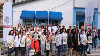 Görselde engelli bireyler yan yana duruyor ve önlerinde tekerlekli sandalye kullanan engelli bir kadın yer alıyor. Herkesin elinde ise bir kağıt poşet var.