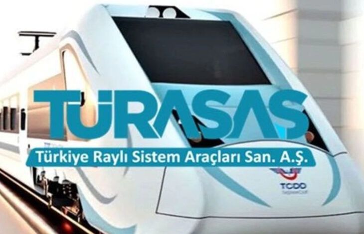 Görselde modern ve aerodinamik tasarıma sahip beyaz bir yüksek hızlı tren bulunuyor. Üzerinde büyük harflerle "TÜRASAŞ" yazısı yer almakta. Altında ise "Türkiye Raylı Sistem Araçları San. A.Ş." ifadesi görülüyor. Trenin ön kısmında TCDD (Türkiye Cumhuriyeti Devlet Demiryolları) logosu mevcut. Arka planda ise hafif bulanık bir tren istasyonu veya tünel çıkışı hissi veren bir görüntü bulunuyor.