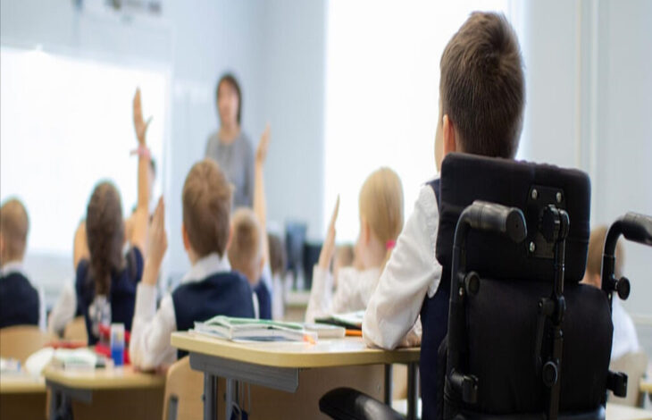 Görselde bir sınıf ortamında sıralarında oturmuş olan öğrenciler olduğu görülmektedir. En arka sırada oturan tekerlekli sandalye kullanıcısı bir öğrenci ise dikkat çekmektedir.