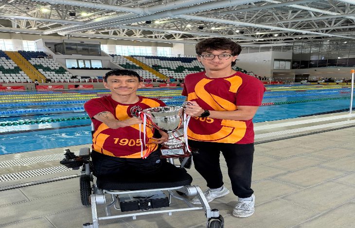 Fotoğrafta, havuz kenarında biri akülü tekerlekli sandalye üzerinde oturan diğeri ise ayakta duran 2 Galatasaray formalı sporcu yer alıyor.