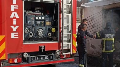 Bu karede Adıyaman İtfaiyesi ekiplerinin bir konteyner kentte çıkan yangına müdahale ettiği görülüyor. Görselin hemen sol tarafında itfaiye aracının arka bölümü, hortum ve kontrol paneli net biçimde seçiliyor. Sağda ise yangın çıkan yapıya yönelen birkaç itfaiye eri bulunuyor. Arka plandaki yoğun duman, olayın ciddiyetini gözler önüne seriyor.