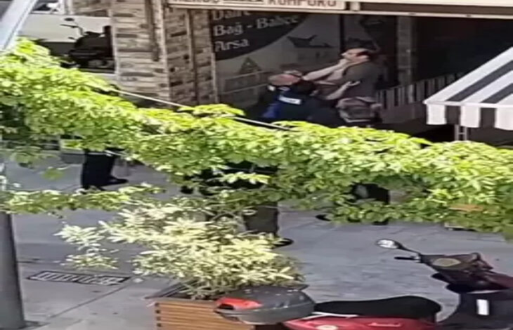 ChatGPT: Görselde, Amasya'nın Merzifon ilçesinde bir sokak görüntüsü yer almakta. Ön planda yeşil sarmaşıklarla kaplı bir yapı dikkat çekiyor. Görselin merkezinde, engelli olduğu anlaşılan bir kişi ile zabıta üniformalı bir görevli arasında fiziksel bir arbede yaşanıyor. Zabıta görevlisi, engelli bireyin boğazına sarılmış gibi görünüyor. Etrafta olaya tanık olan birkaç kişi daha var.