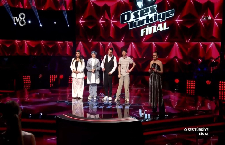 Görme engelli finalist Mert Özer ve diğer ikisi kadın, bir erkek yan yana yarışma sahnesinde bulunuyor.