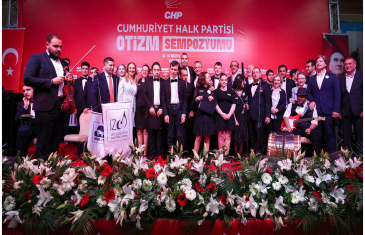 Bu fotoğraf, Cumhuriyet Halk Partisi (CHP) tarafından düzenlenen bir Otizm Sempozyumu etkinliğine ait. Görselde birçok katılımcı, sahnede toplu halde poz verirken görülüyor.