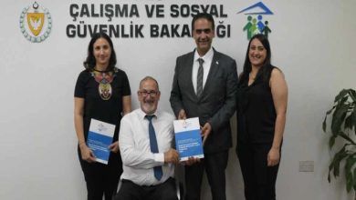 Görselde, KKTC Çalışma ve Sosyal Güvenlik Bakanlığı logosu önünde dört kişi poz vermektedir. Ortada oturan takım elbiseli ve kravatlı bir erkek elinde bir kitapçık tutarken, yanında ayakta duran diğer üç kişi de gülümsüyor. Arka planda bakanlığın adı Türkçe olarak duvarda yer almakta, sol üstte KKTC arması, sağ üstte ise insan figürlü bir logo görülmektedir.