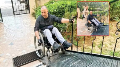 Bu görselde, tekerlekli sandalye kullanan bir birey, apartman girişine yerleştirilmiş eğimli bir metal rampadan inmeye çalışıyor. Rampanın dik ve kaygan olduğu görülüyor, bu da kullanımı oldukça zorlaştırıyor. Küçük ek görselde ise aynı kişi, bir kadının desteğiyle rampayı çıkmaya çalışıyor. Arka planda apartman bahçesi ve yeşillikler yer almakta.