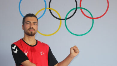 Görselde, kırmızı-siyah Türkiye forması giymiş genç bir erkek sporcu yer almakta. Sol kolu dirsek altından itibaren yok. Arkasında, duvara çizilmiş beş halkadan oluşan olimpiyat sembolü görülüyor. Sporcu, sağ kolunu havaya kaldırarak kararlı ve gururlu bir poz vermiş. Bu duruş, azim, mücadele ve olimpik ruhu simgeliyor. Görsel, engelli bireylerin spordaki güçlü temsilini ve başarıya olan inançlarını etkileyici bir şekilde yansıtıyor.