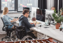 Fotoğrafta bir ofis ortamında çalışan insanlar yer alıyor. Çalışan işçilerden bir tanesi tekerlekli sandalye kullanan engelli birey olması dikkat çekiyor.