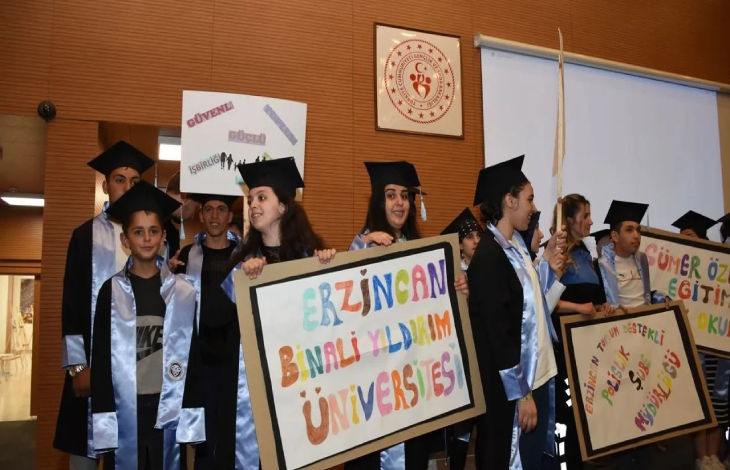 Özel öğrenciler mezuniyet kıyafetleri ve ellerindeki pankartlarla sahnede bulunuyor.