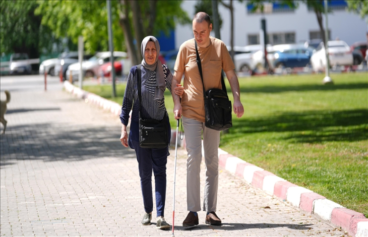 Anne Nevra Yıldırım, beyaz baston kullanan oğlu Önder Savaş Yıldırım ile sokakta kol kola yürüyor.