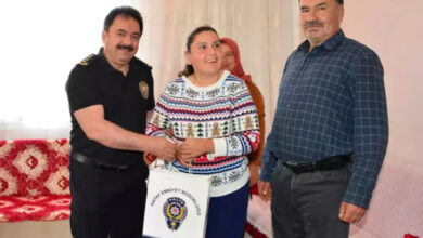 Görselde, bir ev ortamında çekilmiş samimi bir ziyaret anı yer almakta. Solda siyah üniformalı bir polis memuru (muhtemelen Hatay İl Emniyet Müdürü Kadir Gökce), ortada engelli bir genç kızla el sıkışıyor ve ona "Hatay Emniyet Müdürlüğü" logolu bir hediye çantası veriyor. Genç kız neşeli bir şekilde gülümsüyor. Sağda ise muhtemelen kızın babası olan bir adam duruyor; o da tebessüm ediyor. Arka planda bir kadın daha bulunmakta. Mekân sıcak ve sade bir oturma odası havasında.