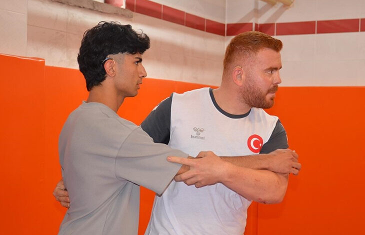 Fotoğrafta, turuncu renkli arka planına sahip kapalı bir spor salonu olduğu düşünülen yerde tekvando yapan 2 erkek görülmektedir. İçlerinden yaşça büyük olduğu düşünülen eğitmen öğrencisine özel bir teknik göstermektedir.