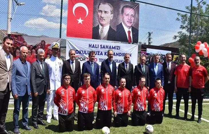 Bu görselde, İzmir'deki Karşıyaka Özel Eğitim Meslek Okulu’nda 10-16 Mayıs Engelliler Haftası kapsamında düzenlenen bir farkındalık etkinliği görülmektedir. Halı saha üzerinde gerçekleştirilen etkinlikte, ön sırada Türk bayraklı kırmızı formalar giymiş, amputee futbolcular diz çökmüş şekilde poz vermektedir. Arkalarında ise sivil ve askerî yetkililer ile öğretmenler olmak üzere çeşitli protokol üyeleri ayakta durmaktadır.