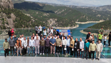 Fotoğrafta işitme engelli bireyler ve aileleri cam bir terasta yan yana durarak toplu bir fotoğraf çekimi için el sallıyorlar.