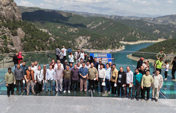 Fotoğrafta işitme engelli bireyler ve aileleri cam bir terasta yan yana durarak toplu bir fotoğraf çekimi için el sallıyorlar.