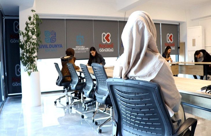 Kapalı bir alanda birkaç kişinin bazı evrak reformları doldurduğu görülmektedir. Ayakta yer alan bir kişide destek amacıyla ihtiyaç duyan kişilere yardımcı oluyor.