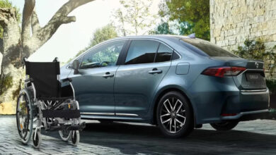 Görselde modern bir otomobilin (Toyota Corolla) hemen önünde duran boş bir tekerlekli sandalye yer almakta. Arka planda taş duvarlı bir ev ve doğa manzarası görülüyor. Fotoğraf, engelli bireylerin mobilite ihtiyaçlarını ve taşıma kolaylığını sembolize ediyor. Aynı zamanda, otomobilin engelli bireyler için önemli bir özgürlük ve bağımsızlık aracı olduğunu da ima ediyor.