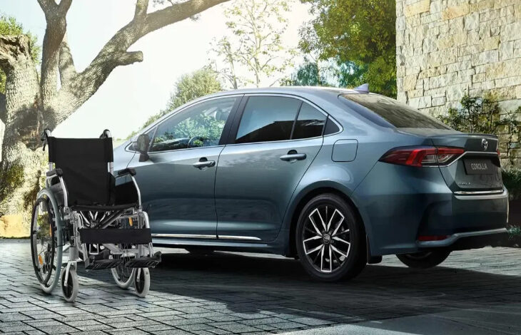 Görselde modern bir otomobilin (Toyota Corolla) hemen önünde duran boş bir tekerlekli sandalye yer almakta. Arka planda taş duvarlı bir ev ve doğa manzarası görülüyor. Fotoğraf, engelli bireylerin mobilite ihtiyaçlarını ve taşıma kolaylığını sembolize ediyor. Aynı zamanda, otomobilin engelli bireyler için önemli bir özgürlük ve bağımsızlık aracı olduğunu da ima ediyor.