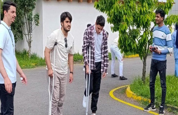 Fotoğrafta bir etkinlik kapsamında koltuk değneği kullanarak yürümeye çalışan üniversite öğrencileri yer alıyor.