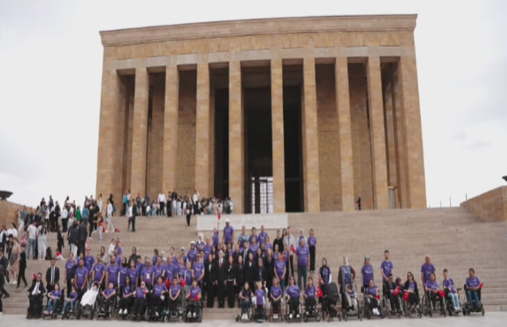 Bu görselde, Anıtkabir'in ön basamaklarında büyük bir grup insan toplanmış. Grup, çoğunluğu mor tişört giymiş bireylerden oluşuyor. Katılımcıların bir kısmı tekerlekli sandalyede. Arka planda Anıtkabir'in sütunlu yapısı belirgin şekilde görülüyor. Görsel, ciddi ve anlamlı bir ziyaretin anısını taşıyor. SMA’lı bireyler ve ailelerinin yer aldığı bir etkinlik kapsamında çekilmiş.