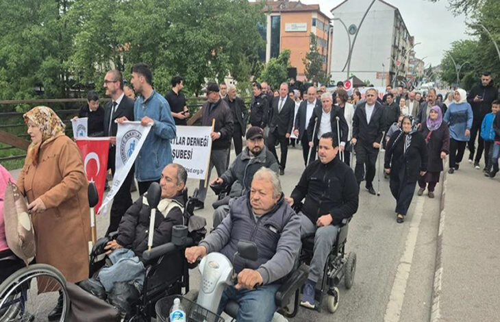 Bu görselde, 10-16 Mayıs Engelliler Haftası kapsamında Bartın'da düzenlenen bir yürüyüş etkinliği görülmektedir. Ön saflarda akülü tekerlekli sandalye kullanan bireyler yer almakta, arkalarında ise çeşitli yaş ve cinsiyetlerden katılımcılar yürümektedir. Katılımcılar arasında Bartın Belediyesi ve dernek üyeleri de bulunmaktadır.