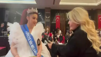 Fotoğrafta, tekerlekli sandalye kullanan iki kadın karşı karşıya duruyor. Sağ taraftaki kadının elinde bir mikrofon var. Sol taraftaki kadının ise üzerinde beyaz bir kıyafet ve “Meleklerin güzellik yarışması” yazısı yer alıyor.