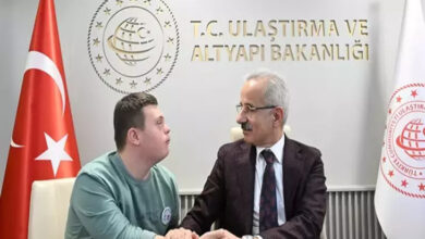 Ulaştırma ve Altyapı Bakanı Abdulkadir Uraloğlu, yanında yer alan Down sendromlu engelli birey ile bir masanın arkasında oturuyor ve konuşuyorlar. Bakanın arkasında ise Ulaştırma ve Altyapı Bakanlığı yazısı var.