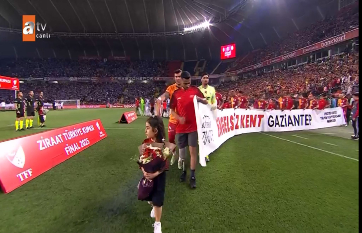 En önde protez bacaklı kız çocuğu elinde çiçekler tutuyor ve arkada Galatasaraylı futbolcular ve engelliler sahaya çıkıyor.