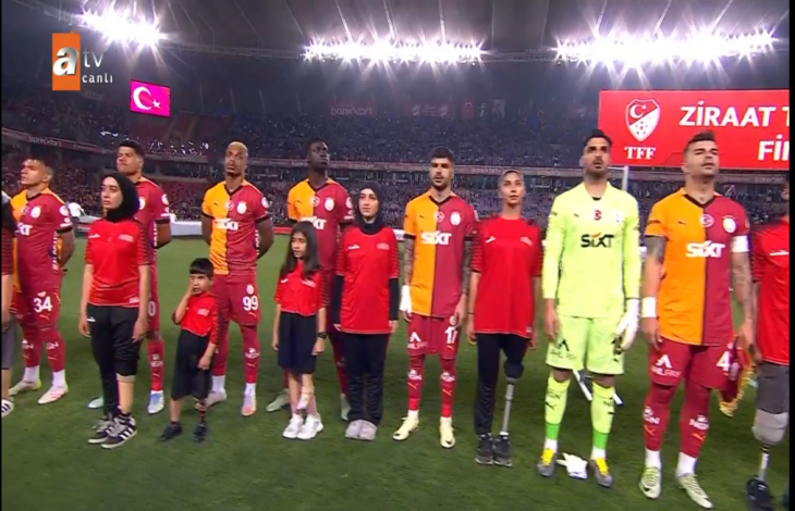 Galatasaraylı futbolcuların yanında bulunan engelliler İstiklal Marşı okunurken seremonide bulunuyor.