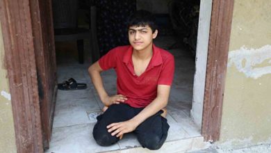 Tekerlekli sandalyesi çalınan Enes, kapı önünde dizlerinin üstünde oturuyor.