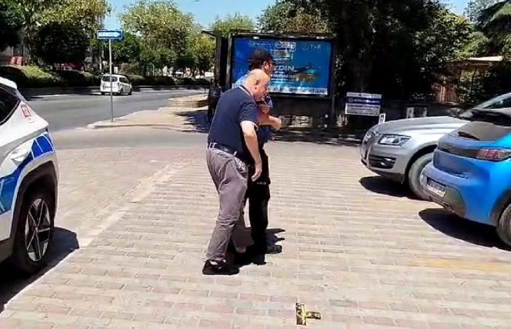 Görselde, Aydın’ın Efeler ilçesinde geçtiği anlaşılan bir olayda, iki görevli erkeğin görme engelli bir bireye yardım ettiği görülüyor. Kaldırımda yürüyen üç kişi bulunmakta; biri rehberlik eden görevli, diğeri görme engelli birey ve diğer kişi de destek sağlıyor. Arka planda park etmiş araçlar ve bir reklam panosu yer alıyor. Yardım edilen bireyin bankaya gitmek üzere çağrı merkezi aracılığıyla destek istediği anlaşılıyor.