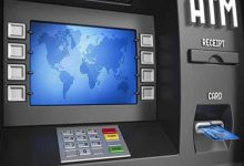 Görselde bir ATM cihazı yer alıyor. Ekranında mavi tonlarda bir dünya haritası görüntülenmiş. Ekranın her iki yanında işlem tuşları bulunuyor. Alt kısımda ise rakam tuş takımı, renkli işlem tuşları (iptal, düzelt, giriş) yer almakta. Sağ tarafta kart giriş yuvasında mavi renkli bir banka kartı takılı duruyor. Ayrıca "RECEIPT" (fiş) ve "CARD" (kart) bölümleri de etiketlenmiş şekilde görülüyor. Görsel, muhtemelen erişilebilirlik özelliklerine sahip yeni nesil ATM'leri temsil ediyor.