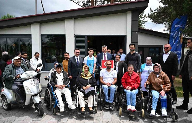 Görselde, Erzurum Valisi Mustafa Çiftçi'nin de aralarında bulunduğu bir grup insan, bir bina önünde toplanmış. Ön sırada tekerlekli sandalye kullanan engelli bireyler oturuyor; arkada ise etkinliğe katılan protokol üyeleri ve diğer katılımcılar yer alıyor. Sağ köşede “Erzurum Büyükşehir Belediyesi” logolu bir bayrak dikkat çekiyor. Etkinlik, Türkiye Sakatlar Derneği Erzurum Şubesi tarafından düzenlenen “Arzuhal Günleri” kapsamında gerçekleşmiş.