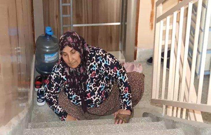 Fotoğrafta, Hatice Avcı isimli engelli birey eline geçirmiş olduğu terliklerle birlikte merdivenler yukarı doğru sürünerek çıkmaya çalışıyor.