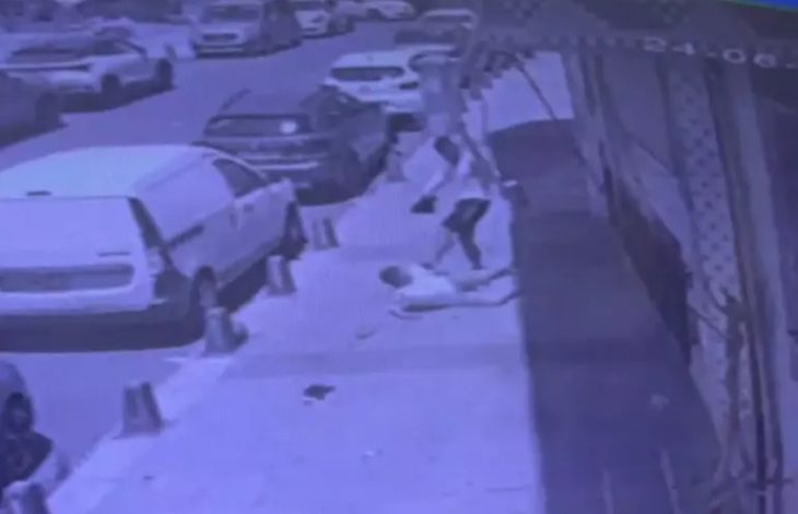 Görselde, kaldırımda yere yatmış şekilde duran bir çocuk ve yaşça daha büyük bir erkek tekme atarak yerde yatan kişiyi darp ediyor.