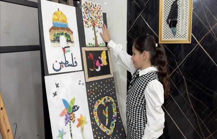 Fotoğrafta, görme engelli bir kız çocuğu resim tablolarının önünde durmuş ve tablolara dokunarak basın mensupları ile konuşuyor.