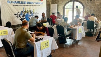 Görselde, taş duvarlı tarihi bir binada düzenlenen satranç turnuvası yer almakta. Masalarda karşılıklı oturan bireyler satranç oynuyor. Turnuvanın “Bu Hamleler Engel Tanımaz” sloganı dikkat çekiyor; afişte “Umuda yol olalım: Engelleri aşan hamleler” yazısı da yer almakta. Etkinlik, görme engelli bireylerin de katılım sağlayabildiği kapsayıcı bir organizasyon izlenimi veriyor. Masa numaraları ve su şişeleri, profesyonel bir turnuva ortamını yansıtıyor.