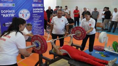 Görselde, Kırıkkale'de düzenlenen Bedensel Engelliler Halter Türkiye Şampiyonası’ndan bir an görülüyor. Kırmızı formasıyla bir sporcu bench press yaparken, etrafında antrenörler ve destek ekibi dikkatle bekliyor. Arkada “Dopinge Hayır” yazılı bilgilendirici pankartlar ve izleyiciler yer alıyor.