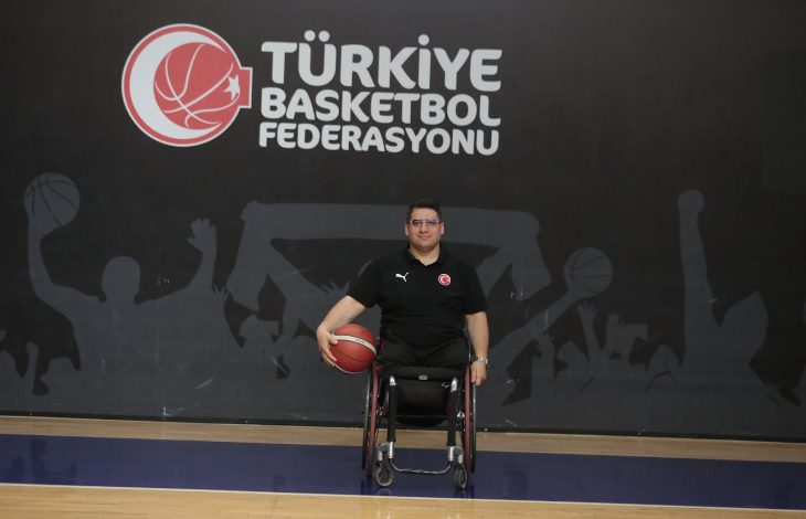 Görselde, Türkiye Basketbol Federasyonu logosunun önünde bir basketbol sahasında poz veren bir erkek yer alıyor. Tekerlekli sandalyede oturan bu kişi, elinde bir basketbol topu tutmakta ve milli takım formasını giymiş durumda. Arka planda spor temalı bir siluet duvar resmi bulunuyor.