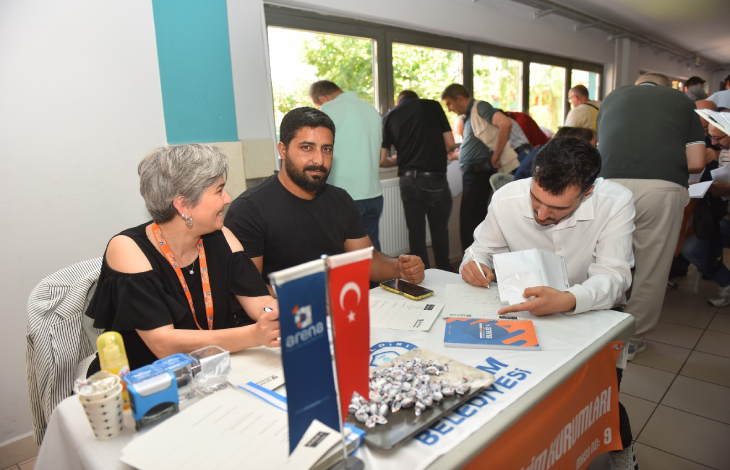 Bir kadın ve bir erkek İnsan Kaynakları personeli yanında iş formu dolduran engelli erkek aday.