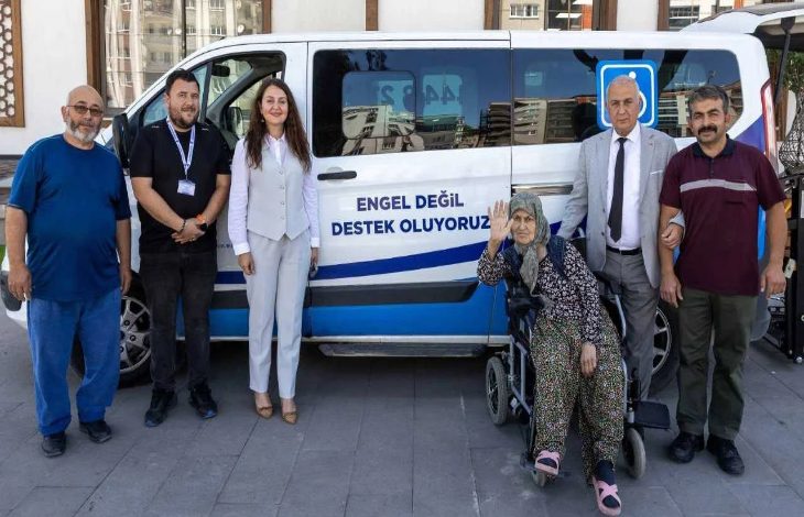 Görselde, Yunus Emre Belediyesi'ne ait olduğu düşünülen transport tipi bir aracın önünde, akülü tekerlekli sandalye kullanan yaşlı bir kadın ile belediye yetkilileri yer alıyor.