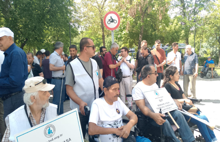 Türkiye Sakatlar Derneği üyesi engelliler dövizler tutarak yan yana bulunuyor.