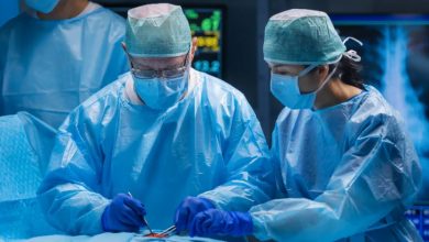 Mavi bone, maske, eldiven ve önlük giyinen iki doktor ameliyat operasyonu yaparken.