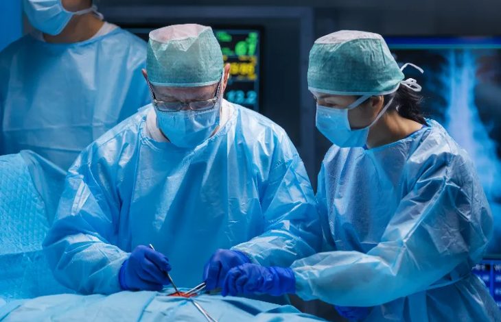 Mavi bone, maske, eldiven ve önlük giyinen iki doktor ameliyat operasyonu yaparken.
