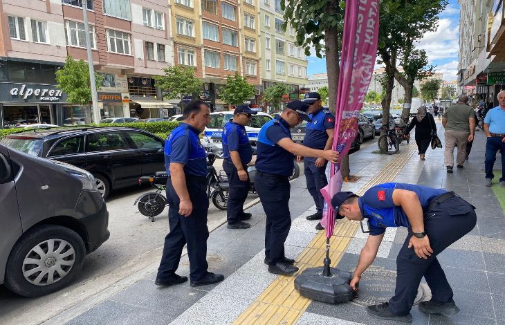 Görselde, Çorum Belediyesi Zabıta Müdürlüğü ekipleri bir kaldırımda denetim yapıyor. Zabıta ekipleri, sarı kılavuz çizgilerin yani görme engelli yolunun üzerine yerleştirilmiş bir tanıtım afişini kaldırıyor. Bu afişin görme engelliler için yapılmış yürüyüş yolunu kapattığı görülüyor. Arka planda apartmanlar, dükkânlar ve park etmiş araçlar yer almakta.
