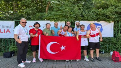 Down Sendrom Atletizm Milli Takımının erkek sporcuları teknik kafile ile Türk Bayrağını tutarak poz veriyor.