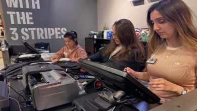 Görselde bir spor mağazasının kasiyer bölümünde çalışan üç kadın personel yer almakta. Hepsi üniformalı ve bilgisayar ekranlarıyla meşgul, dikkatli ve odaklanmış şekilde görevlerini yerine getiriyorlar. Ön planda kasa sistemleri, pos cihazı ve bir yazıcı yer alıyor.