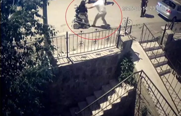 Görselde, bir sokak kamerası görüntüsünden alınmış bir an yer alıyor. Tekerlekli sandalyedeki bir kadına, arkasından yaklaşan bir erkek fiziksel müdahalede bulunuyor. Olay, gece vakti bir kaldırımda geçiyor ve görüntüdeki kişiler kırmızı daire içine alınmış.